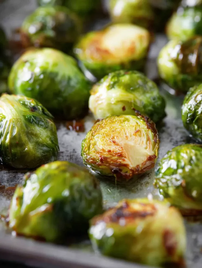 A close-up shot of perfectly roasted brussels sprouts on a silver baking sheet, glistening with oil.