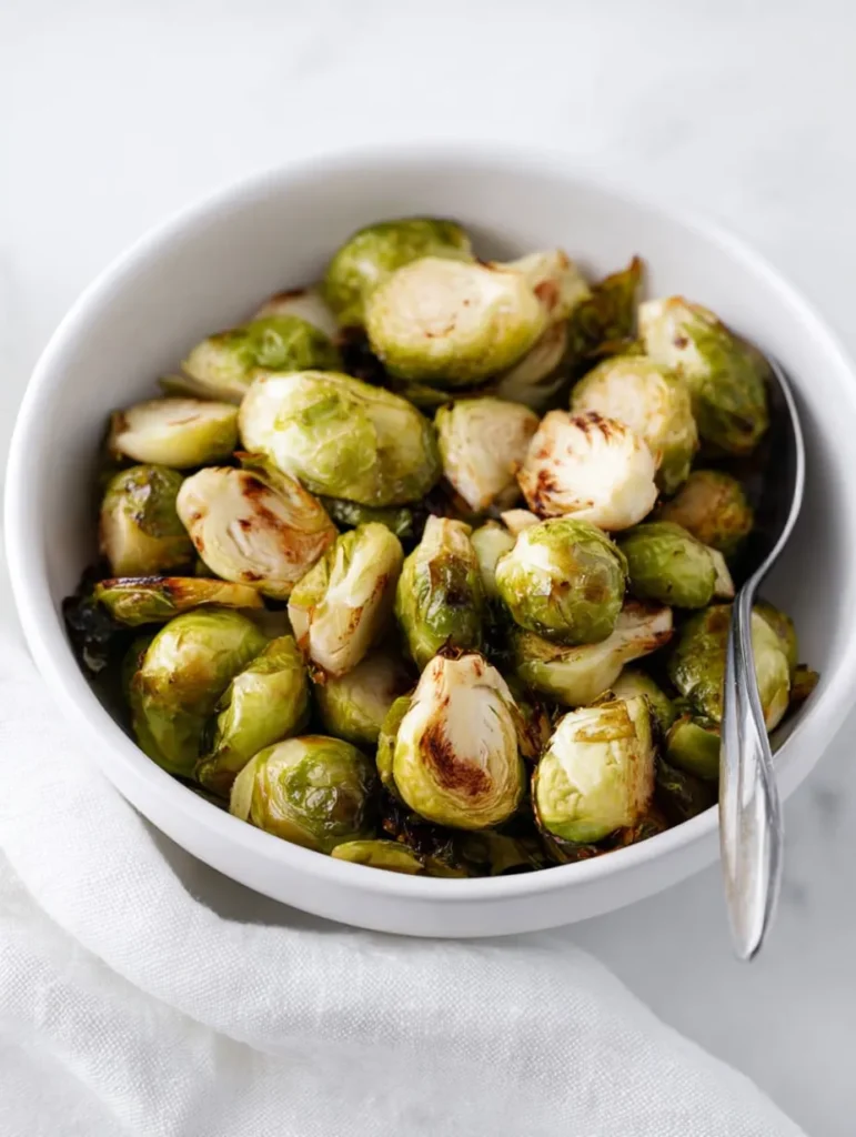 A white bowl filled with perfectly roasted brussels sprouts, featuring golden-brown edges and a spoon.